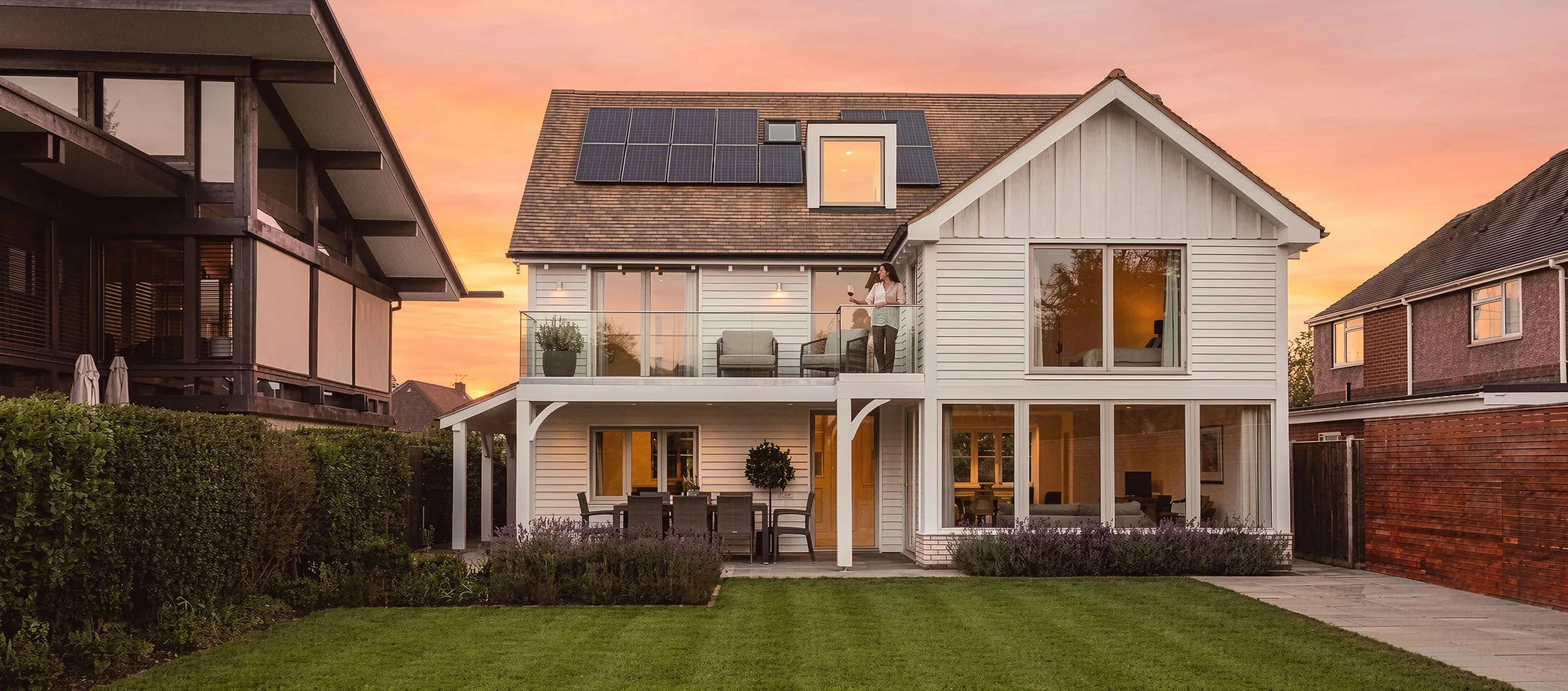 CGI render of Beachfield at Bembridge at sunset, the white weatherboarded rear elevation with a first-floor balcony and covered patio above the garden
